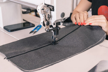 The seamstress sews at the sewing machine, threads the fabric. Women's hands
