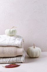 A stack of knitted sweaters on a beige background with pumpkins