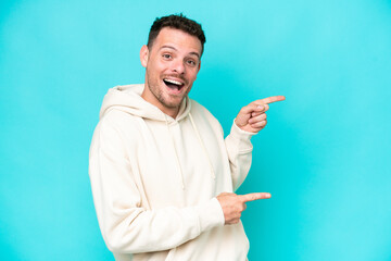 Young caucasian handsome man isolated on blue background surprised and pointing side