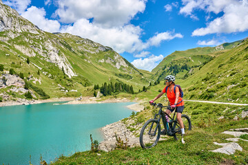 active senior woman, riding her electric mountain bike at Spuller Lake in the Arlberg area near the famous village of Lech, Tirol, Austrian Alps - obrazy, fototapety, plakaty