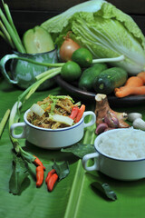 Indonesian specialties, fried vermicelli with rice in a white bowl on a banana leaf with vegetables and seasonings as garnish