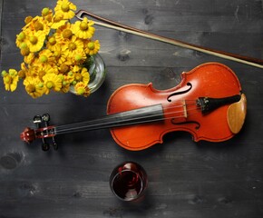 violin, bow, yellow flowers boquet and glass of cognac on black wooden background