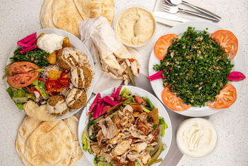 Middle eastern or arabic dishes and assorted meze, white table background. falafel, chicken shawarma sandwich, chicken plate, hummus, tabbouleh, tabouli, Lebanese bread, Halal food. Lebanese cuisine