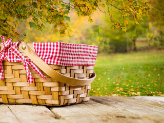 A wicker picnic basket on a wooden table against the backdrop of a wonderful autumn nature. Family vacation, vacation with friends, romantic date, harvest day, thanksgiving day.