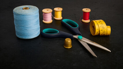 Thimble, scissors, tailor's meter and bobbin with thread on black table, shallow depth of field