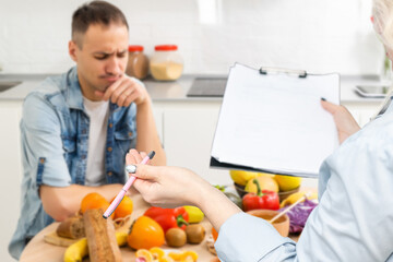 A smiling nutritionist advises a patient on proper nutrition and dieting. The doctor shows a scheme of weight loss without a bad effect on health