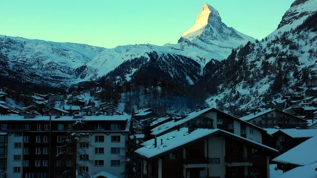 Aerial Upward Shot Of Snow Covered Houses In Town By Mountains Against Clear Sky - Zermatt, Switzerland
