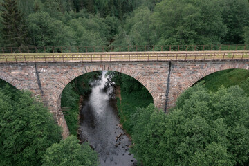 Stone bridge over small river on abandoned railway densely overgrown with grass and trees