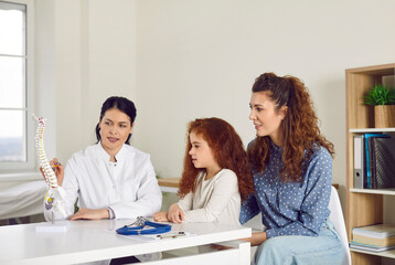 Patients visit doctor at orthopedic clinic. Female medic shows anatomical spine model. Mum and child listen to specialist tell about spinal scoliosis curvature and back and skeleton problem prevention