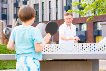 father and son play table tennis. dad teaches the child to play ping pong, father's day, healthy...