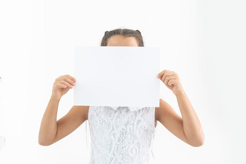 Clean sheet of a paper in child's hands covering her face on white background. Mockup sheet of paper in child's hands.