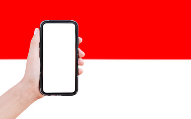 Close-up of male hand holding smartphone with blank on screen, on background of blurred flag of Indonesia.