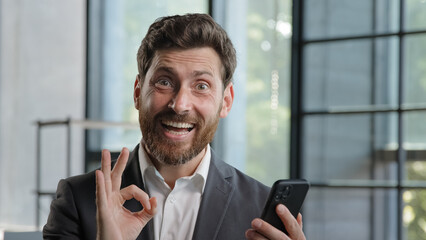 Caucasian bearded businessman 40s boss leader in office with mobile phone victory triumph win...