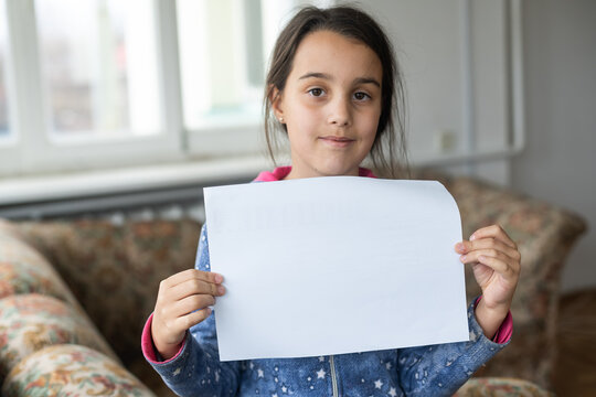 Conceptual image of a sad dejected little girl, holds a blank sheet of paper on gray background.