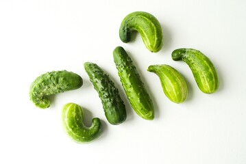 Green cucumbers of different sizes and shapes lie in a chaotic manner on a white isolated background.  Lack of fertilizer during the ripening period.  Close-up.  Flat lay.