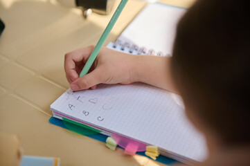 View from above with details on the hand of schoolchild, first grader holding a pencil and learning...