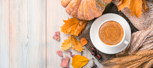 Autumn background with coffee mug, pumpkin and autumn foliage on a holy wooden background. Top...