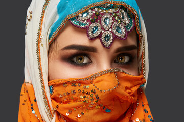 Studio shot of a chrming female wearing the colorful hijab decorated with sequins and jewelry. Arabic style.