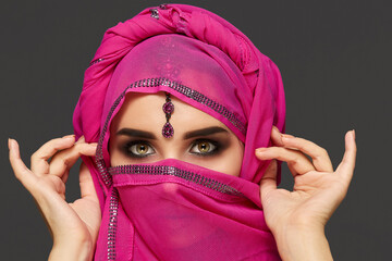 Close-up shot of a young charming woman wearing the pink hijab decorated with sequins and jewelry....