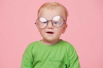 Portrait of male baby boy on pink background wearing glasses and looking at the camera. Smart baby...