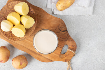 Vegan potato milk in glass and potato in plate on wooden board. Plant based milk replacer and lactose free