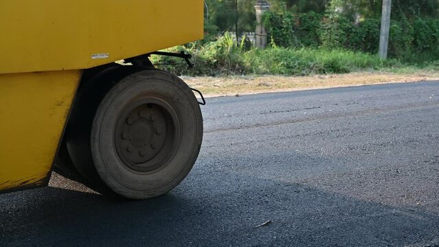 Yellow steamroller or soil compactor working on asphalt road at construction site