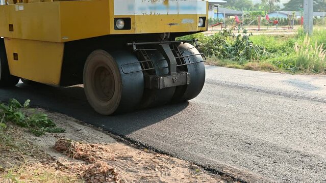Yellow steamroller or soil compactor working on asphalt road at construction site
