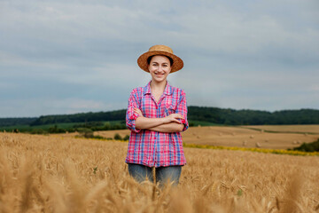Obraz premium Young farmer woman in straw hat and checkered shirt on wheat ripe golden field. Agriculture. Wheat ripens