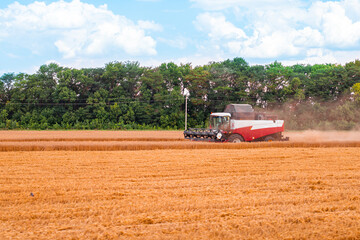 The harvester works on an agricultural field harvests wheat on a sunny day