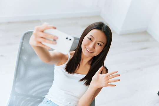 Enjoyed smiling tanned lovely young Asian woman waving hand greeting friend on live doing selfie video call at home. Distance communication Social media concept. Cool offer Banner Wide angle