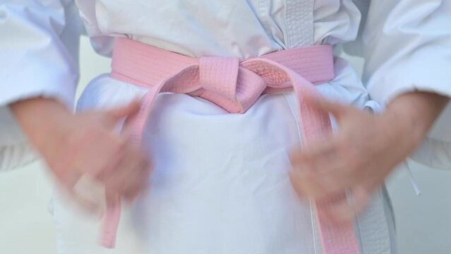 Unrecognizable woman in a pink head covering and a karate suit with a pink belt. She fights cancer concept.
