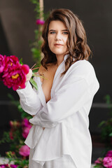 An attractive and peaceful brunette woman in white clothes with peonies.