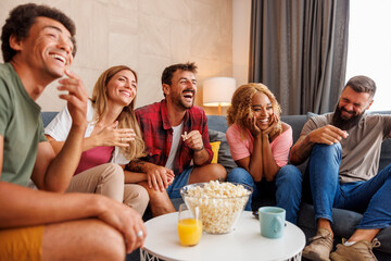Friends lauging and eating popcorn while watching funny movie on TV