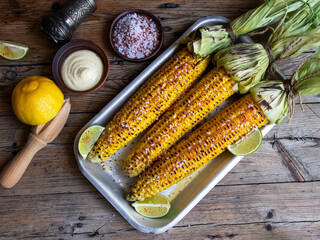 three heads of yellow corn grilled lemon lime spicy white sauce rustic style on a wooden surface top view
