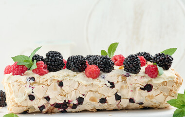 Baked meringue roll with cream and fresh fruits on a white wooden board, delicious dessert