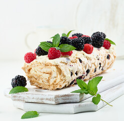 Baked meringue roll with cream and fresh fruits on a white wooden board