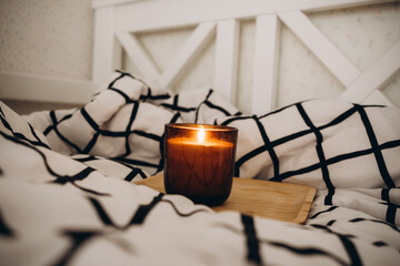 eco soy candle in a glass brown holder on a wooden tray in a black and white bed