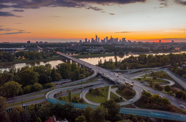 Obraz premium Stunning sunset skyline, aerial view Warsaw, Poland. Drone shot of city downtown business center skyscrapers in background. Highway bridge over river and driving cars, amazing cloudscape evening dusk