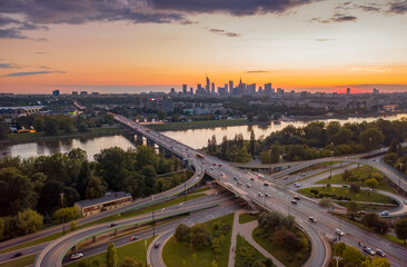 Stunning sunset skyline, aerial view Warsaw, Poland. Drone shot of city downtown business center skyscrapers in background. Highway bridge over river and driving cars, amazing cloudscape evening dusk