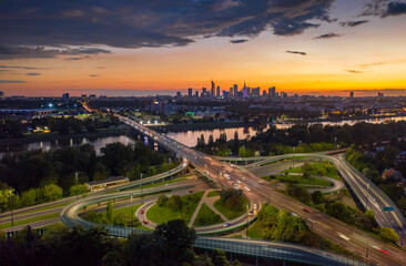 Stunning sunset skyline, aerial view Warsaw, Poland. Drone shot of city downtown business center skyscrapers in background. Highway bridge over river and driving cars, amazing cloudscape evening dusk