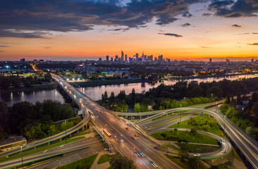 Stunning sunset skyline, aerial view Warsaw, Poland. Drone shot of city downtown business center skyscrapers in background. Highway bridge over river and driving cars, amazing cloudscape evening dusk - obrazy, fototapety, plakaty