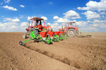Farmer with tractor sowing on agricultural field on sunny spring day