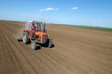 Fototapeta premium Farmer with tractor sowing on agricultural field on sunny spring day