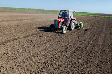 Farmer with tractor sowing on agricultural field on sunny spring day