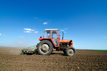 Fototapeta premium Farmer with tractor sowing on agricultural field on sunny spring day