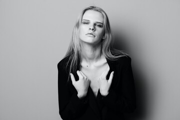 Gorgeous young stylish lady in jacket posing leaning on the wall at studio. Pretty female blonde model sexy looking at camera