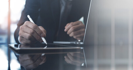 Close up of businessman using stylus pen signing business contract on digital tablet, working on laptop computer at office, e-signing, electronic signature