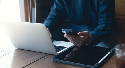 Man freelancer working on laptop and using mobile phone on wooden table at coffee shop, telecommuting