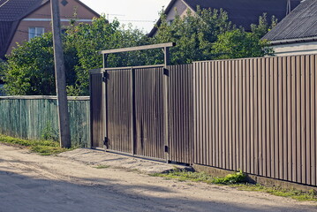 one big closed metal black gate and part of a iron fence wall on a rural street
