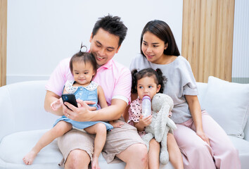 Asian parents with kids on couch using gadget. Young man and woman with son and daughter spending time together with phone .Father and mother watching something online on computer. Rest at home.